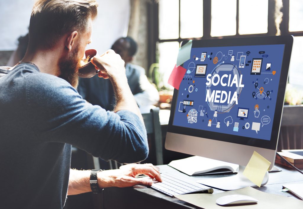 Mann drikker kaffe og jobber på data hvor det står Social Media