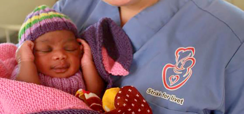 Bilde av en baby i strikketøy som blir holdt av en sykepleier i uniform hvor det står "Strikk for livet"