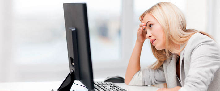 Oppgitt kvinne ser på datamaskin og holder seg for pannen
