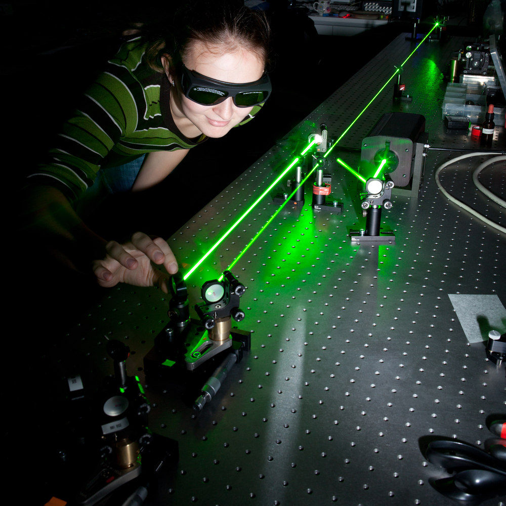 Jente med sikkerhetsbriller ser på grønn laserstråle og justerer refleksjonen til strålen