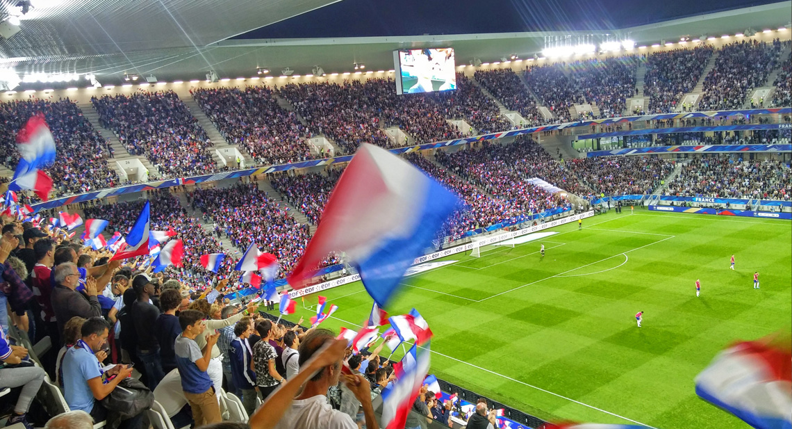 Full tribune av folk som vifter med franske flagg på fotballkamp