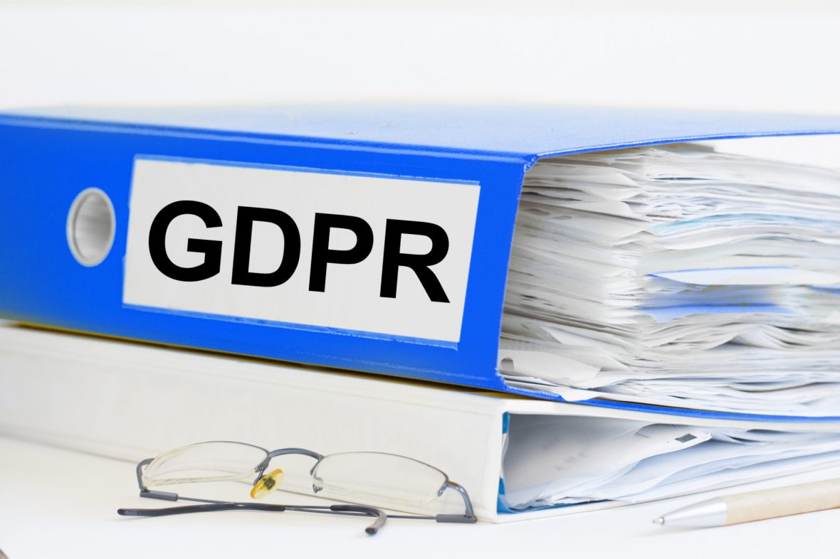 En blå perm hvor det står "GDPR" ligger på en hvit perm bak et brillepar