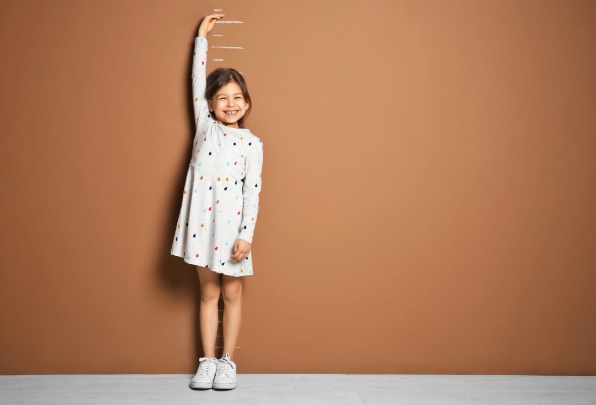 Ung jente står foran brun vegg og måler høyden sin