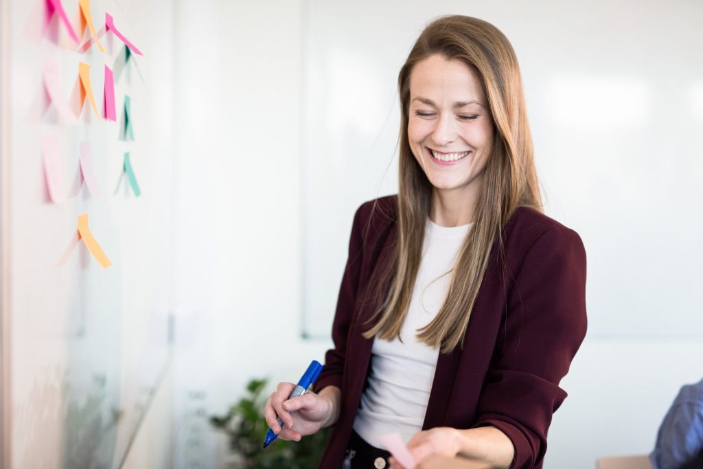 Smilende kvinne setter post-it lapper på et whiteboard
